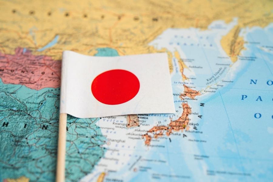 Un mic steag al Japoniei stă înfipt pe o hartă geografică a Asiei de Est, indicând poziția țării în Oceanul Pacific.